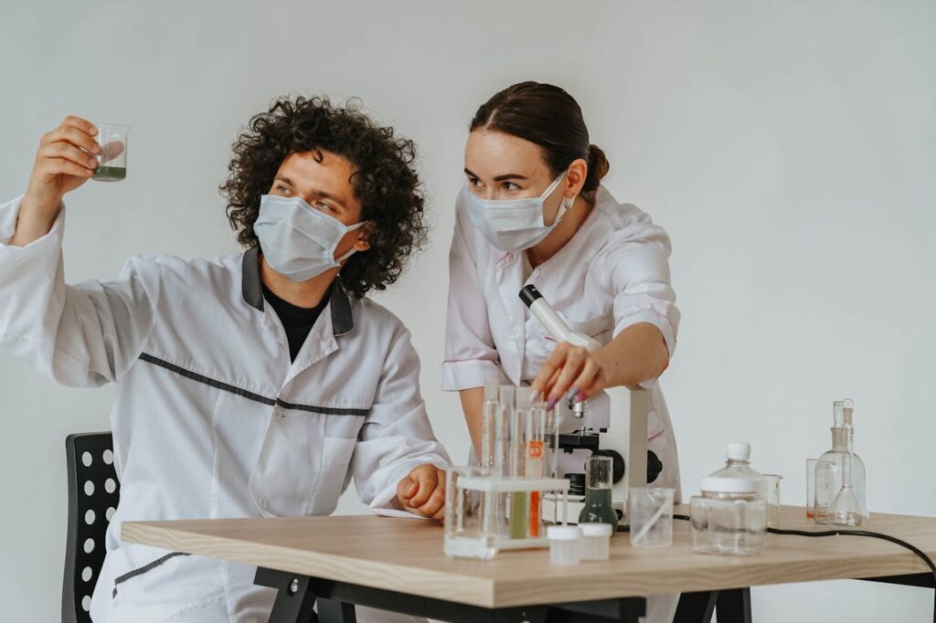Scientists in protective masks conduct research with a microscope and test tubes.