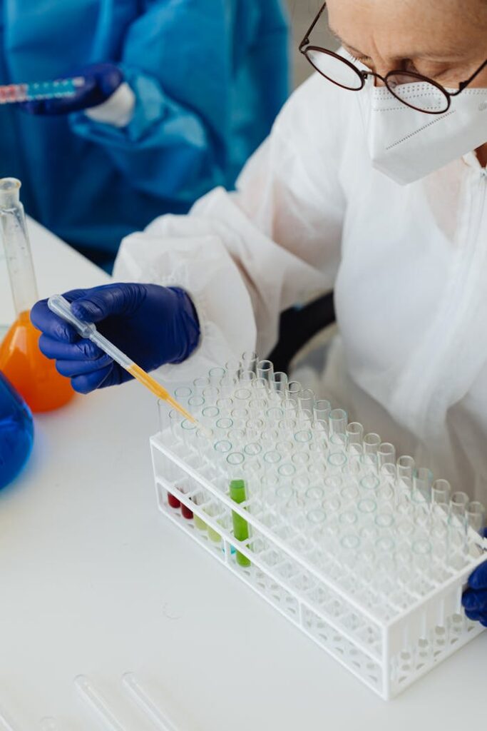 Scientist in protective gear using pipette with test tubes in a lab setting.