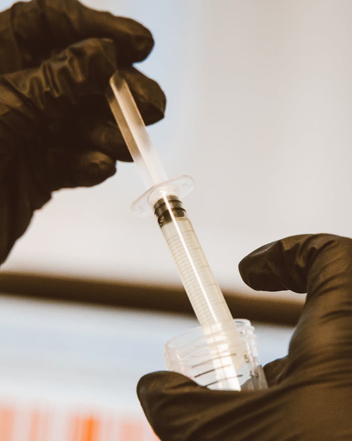 Close-up of a syringe handled with black gloves in a laboratory setting.
